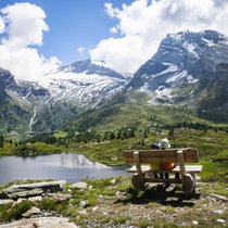 Besonders für Familien ist die Bergalpeam Simplon ein ideales Wandergebiet. Die beiden jungen Wanderer geniessen die Pause auf einem Bänkli am Weg.Über dem Hopschusee erhebt sich der Monte Leone, rechts davon zeigt sich das Hübschhorn.