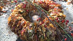 Der Kranz macht Ordnung im herbstlichen Laubhaufen. Eine Kerze in der Mitte lässt die filigranen Blätter leuchten.