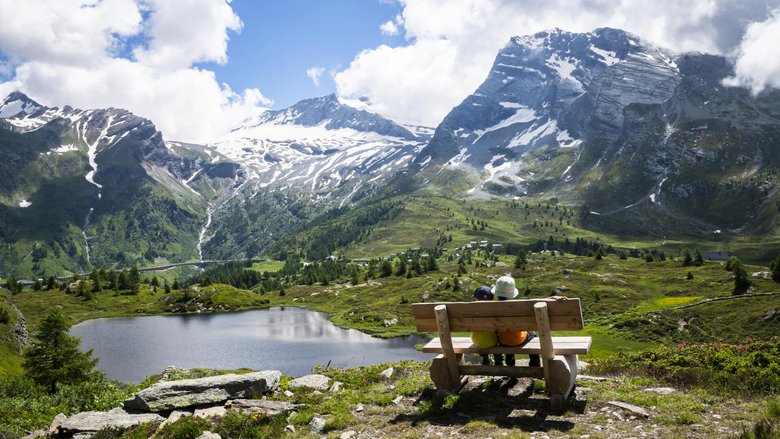 Besonders für Familien ist die Bergalpeam Simplon ein ideales Wandergebiet. Die beiden jungen Wanderer geniessen die Pause auf einem Bänkli am Weg.Über dem Hopschusee erhebt sich der Monte Leone, rechts davon zeigt sich das Hübschhorn.