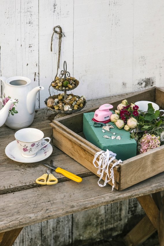 Material Blumengesteck: Tasse, Schere, Steckschwamm etc. in Holzkiste arrangiert