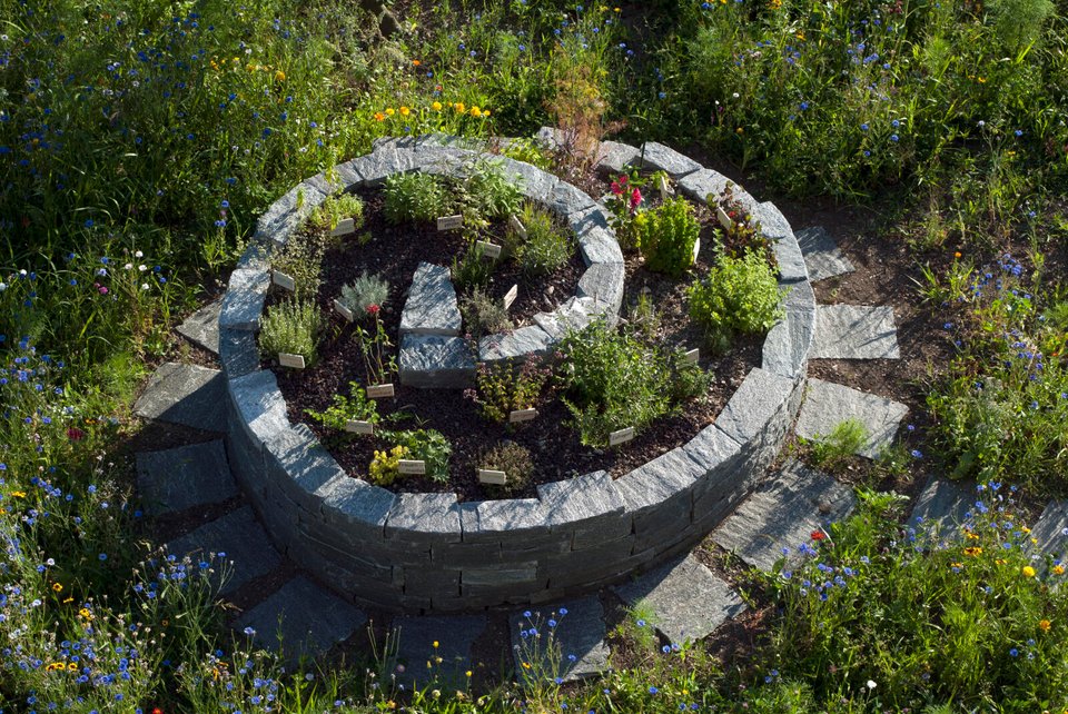 Kräuterspirale LandLiebe-Garten umgeben von blühenden Blumen